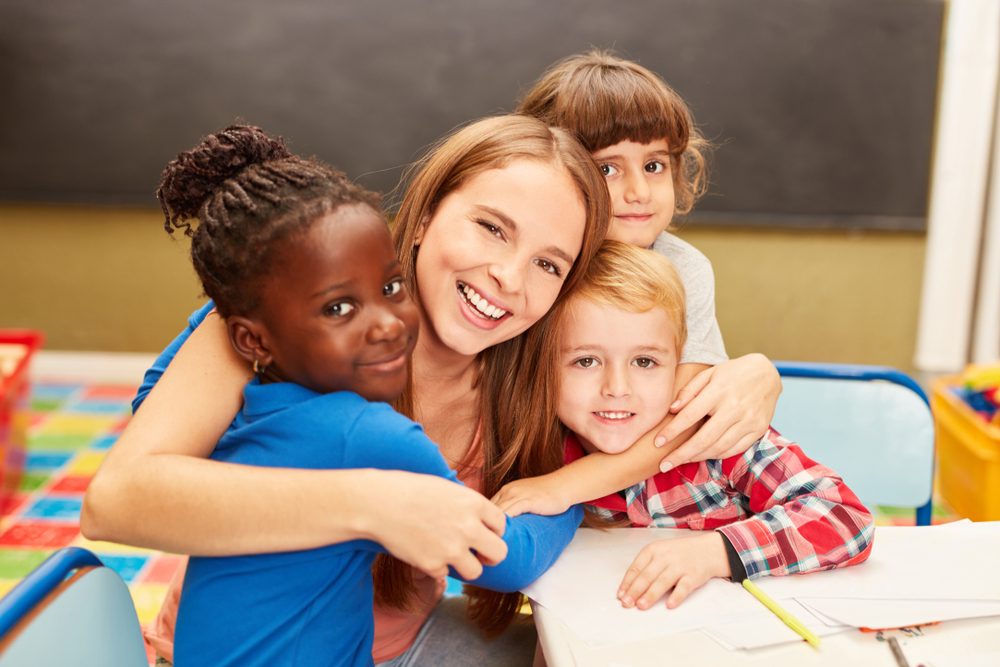 Preschool teacher surrounded by children and receiving hugs